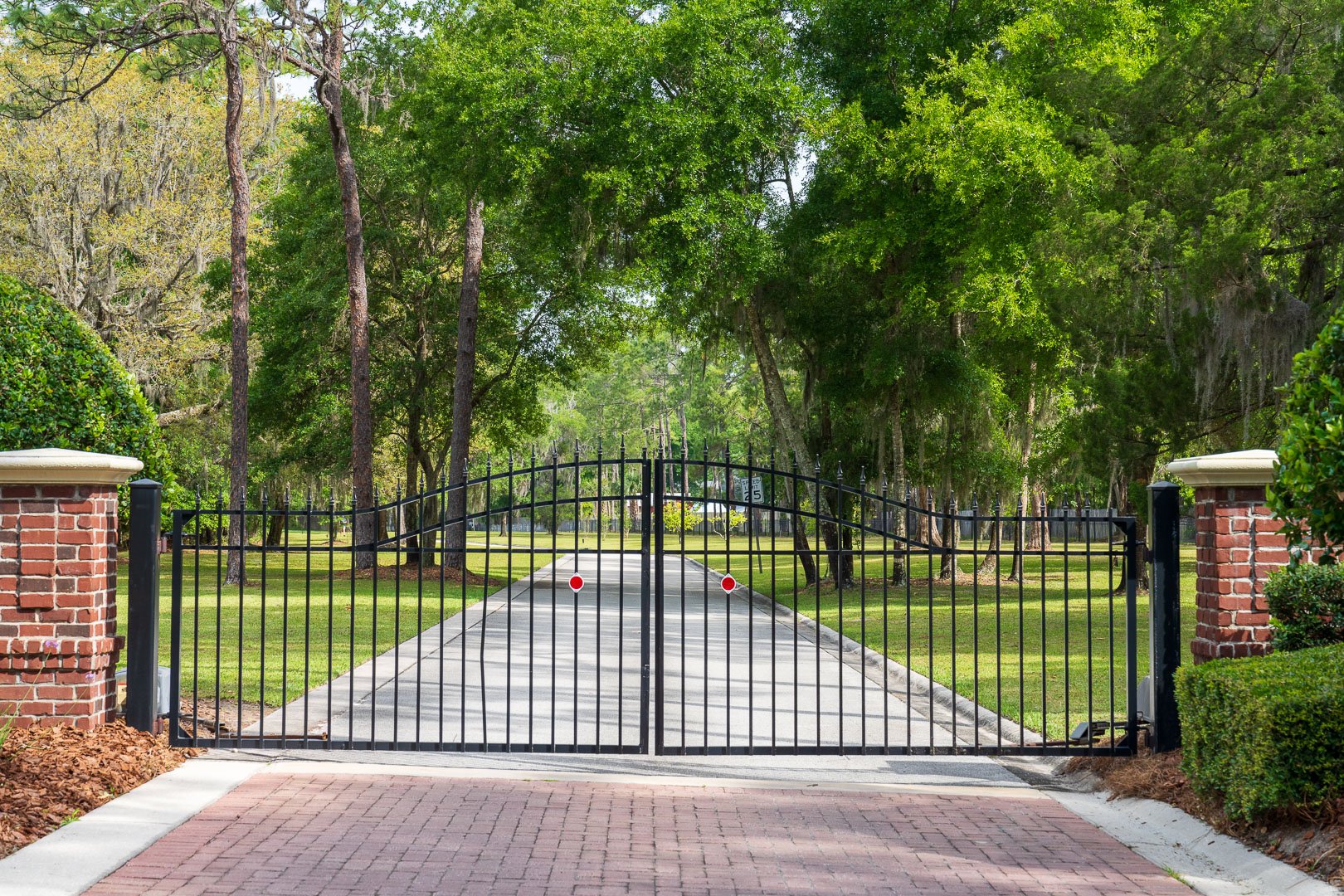 maintenance driveway entrance gate with nice lawn and large trees