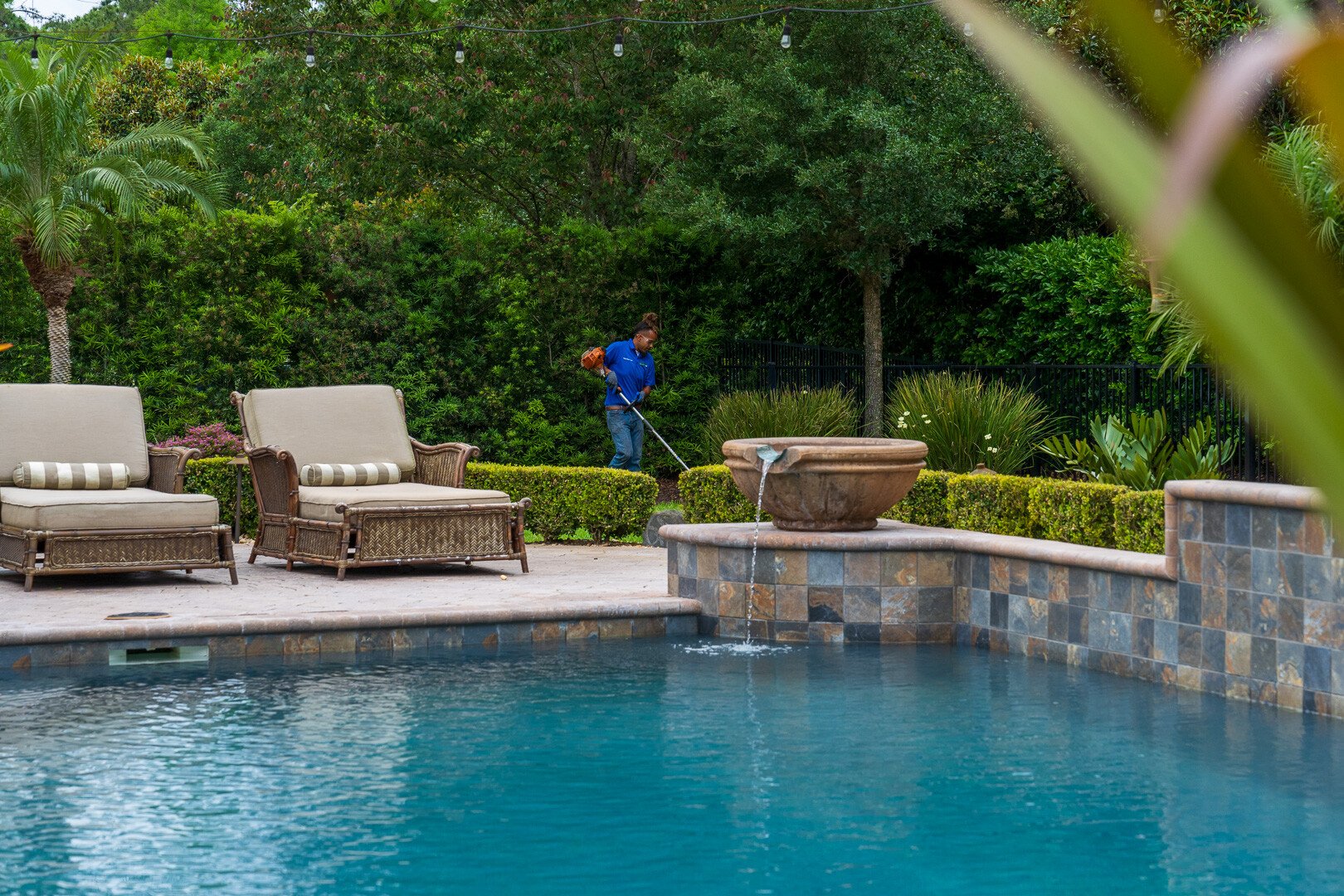 residential maintenance technician edging planting beds near pool